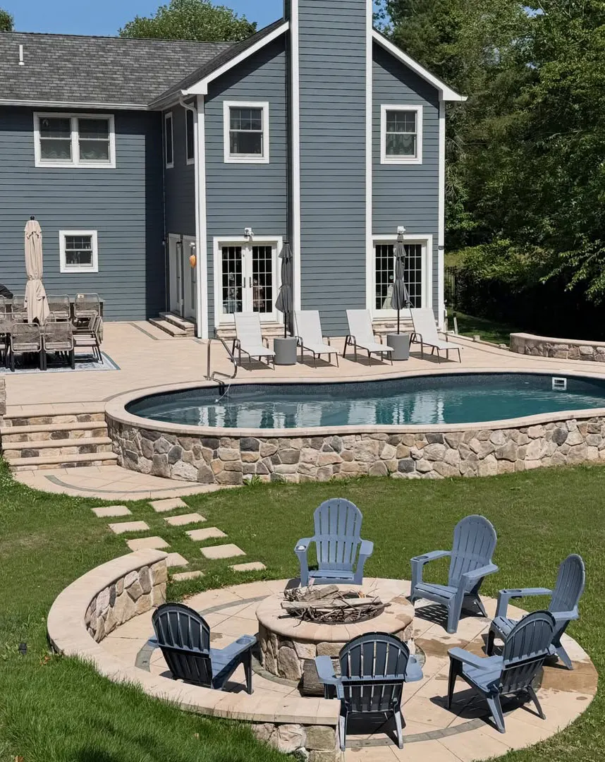 Long Island backyard masonry project with pool patio, stone retaining walls, paver seating area, and fire pit